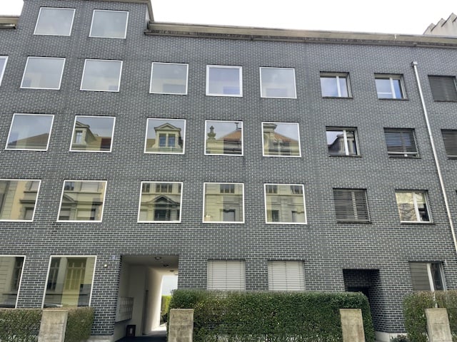 Gray brick building, 6 stories, many glass windows, entrance passageway