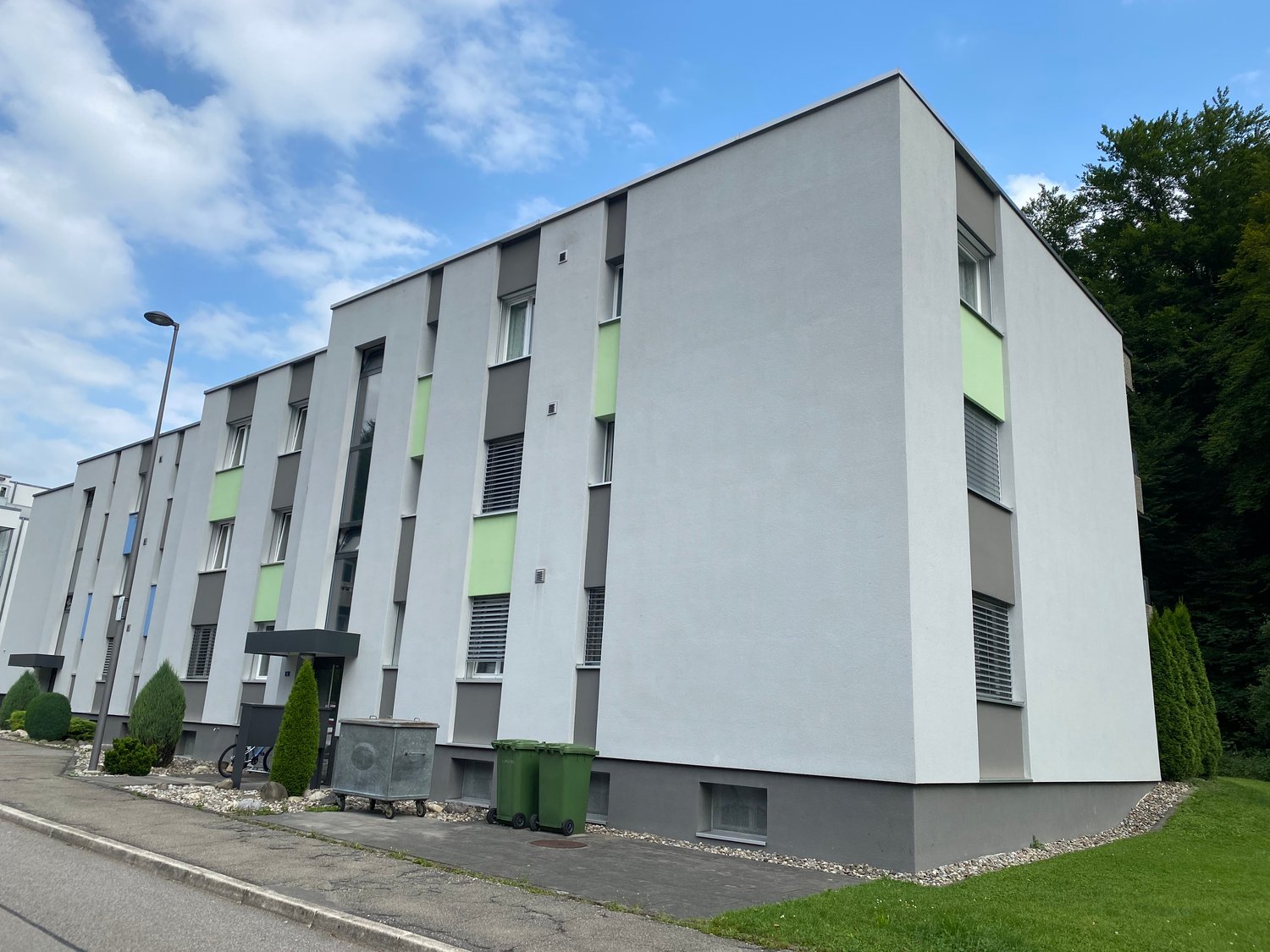 Modern apartment building with gray and green exterior, multiple windows, and a flat roof.