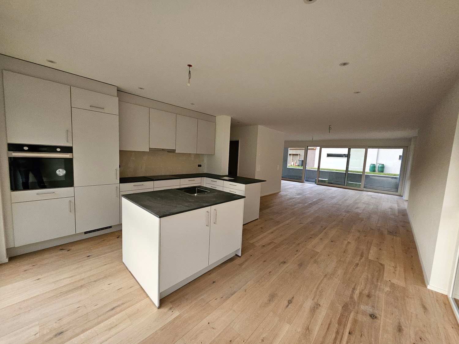 modern kitchen with white cabinets, black countertops, glass sliding doors, wooden floor