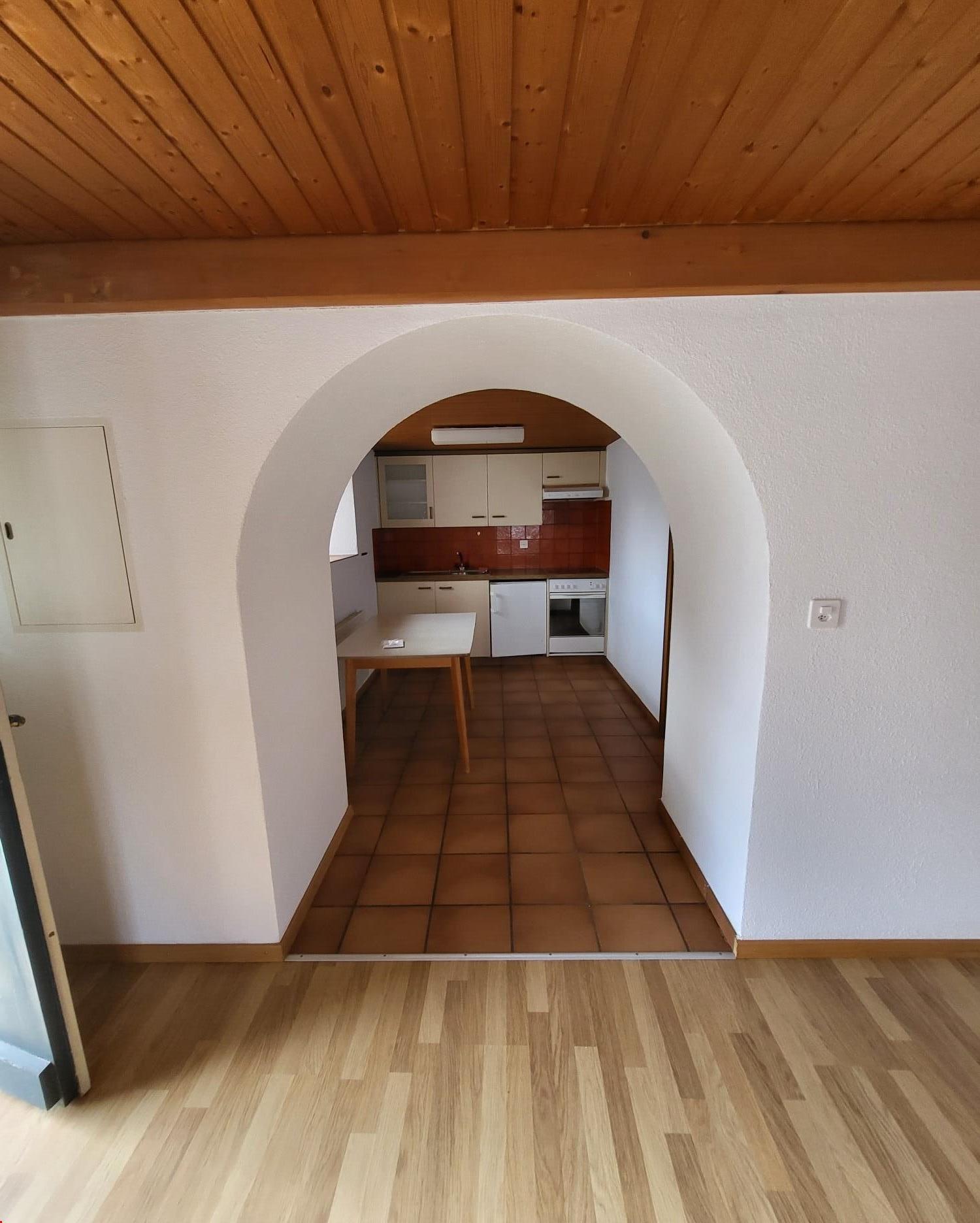 Wooden arch, wooden floor, tiled floor, open kitchen with appliances, wooden door, white walls, wooden ceiling