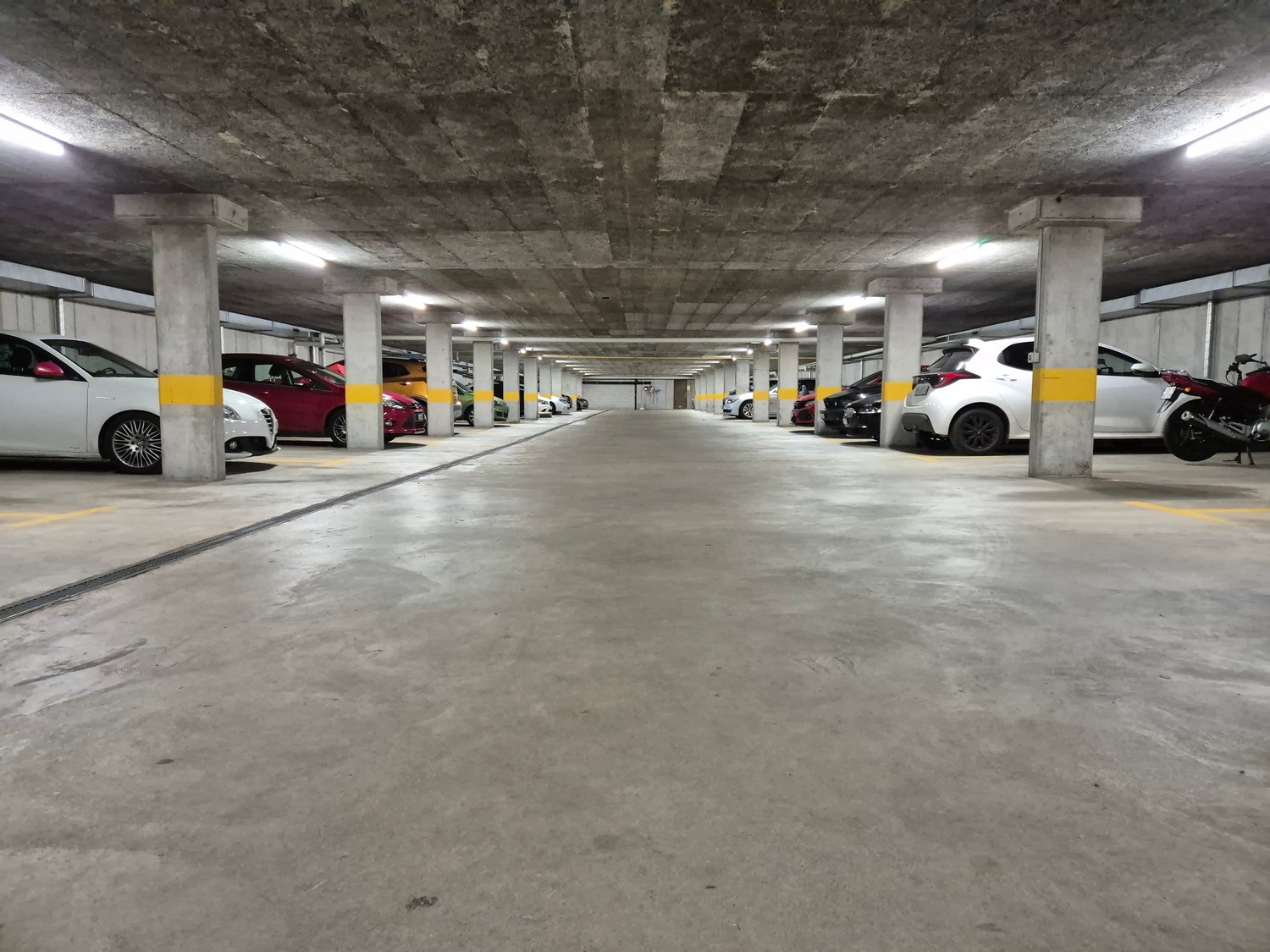 Underground parking garage with concrete ceiling and columns, lined with parked cars on both sides