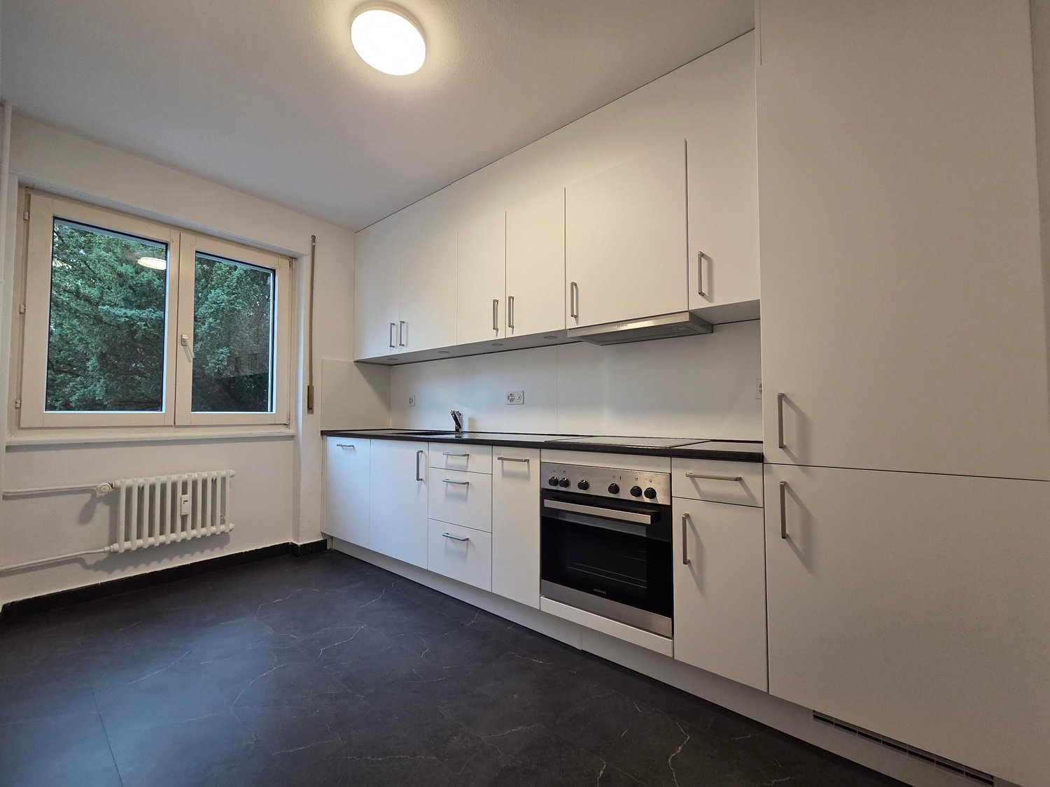 clean kitchen with white cabinetry, black tile flooring, central island with sink and oven, double windows