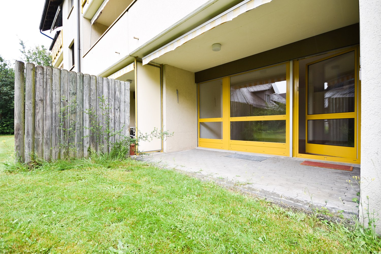 white building with yellow doors, raised ground floor, wooden fence