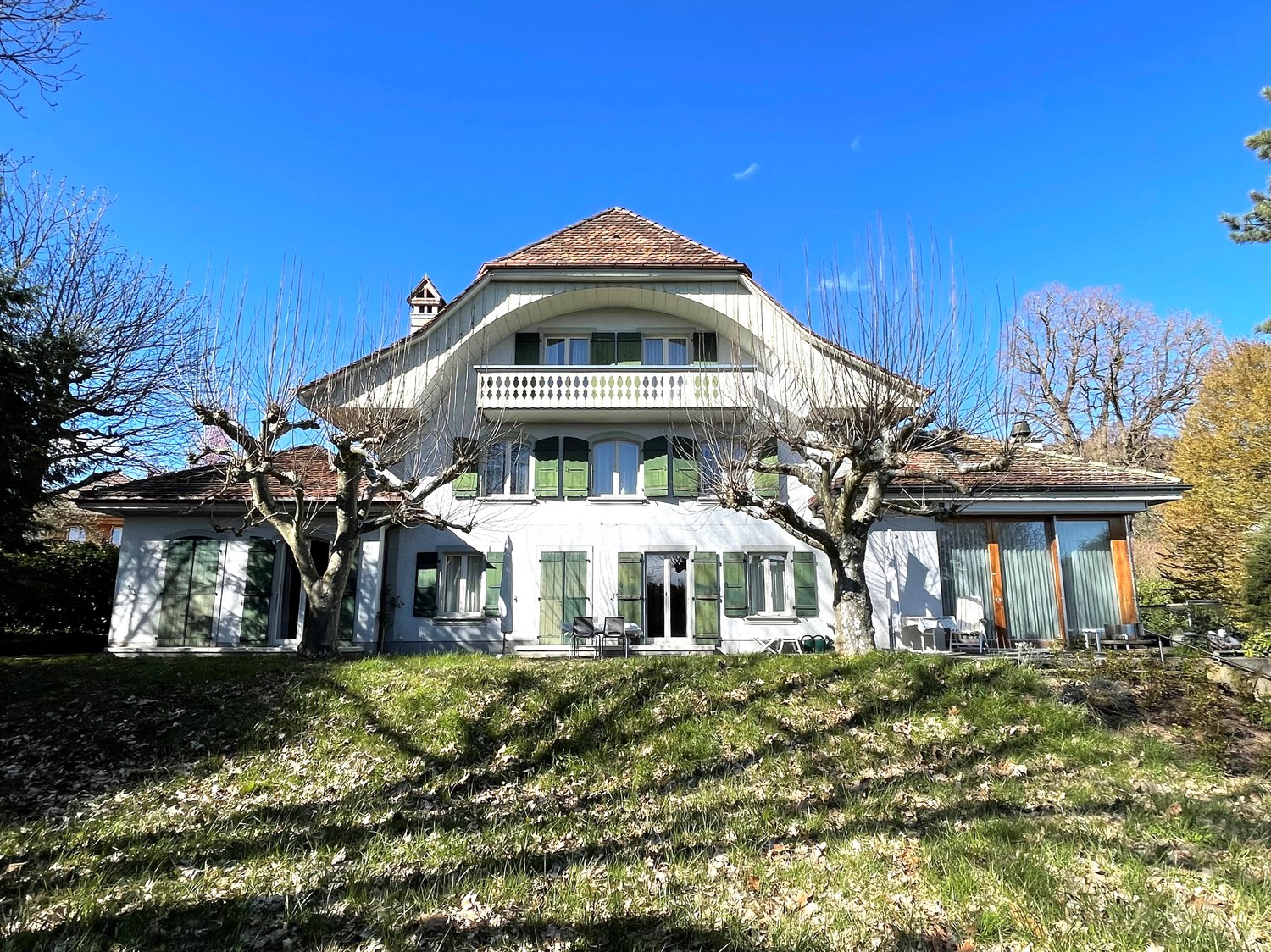 2 story house, white exterior, green shutters, brown roof, large balcony, garden