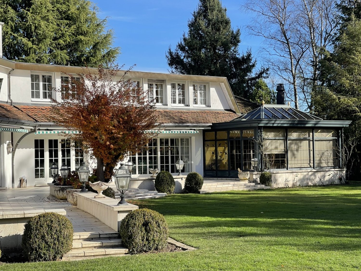 large villa, multiple windows, glass conservatory, manicured lawn, garden features, large driveway