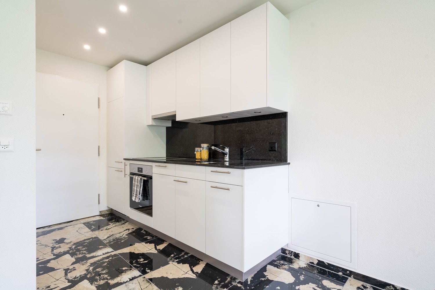 modern kitchen, white cabinets, black countertops, stainless steel appliances, black and white tiled flooring