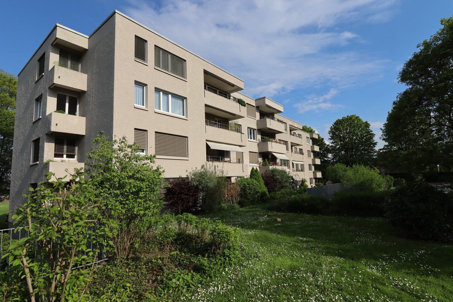 Modern multi-story building with balconies, large lawn in front, several trees