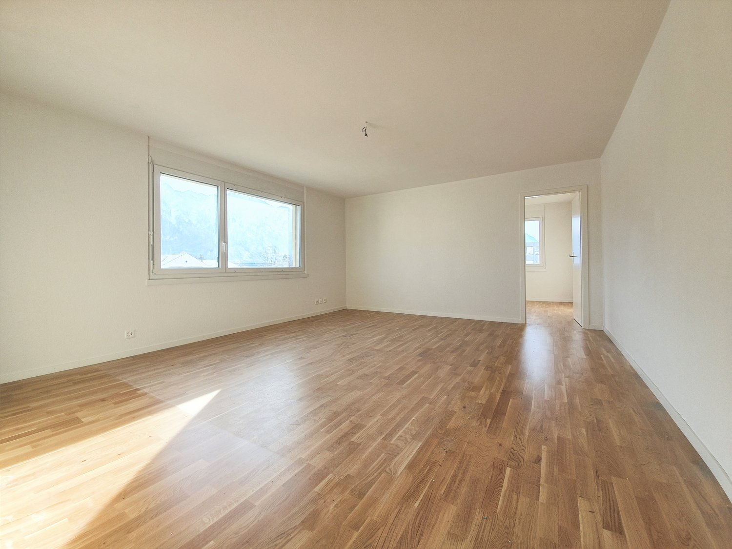Large empty room, hardwood floors, windows, doorway to another room, sunlight