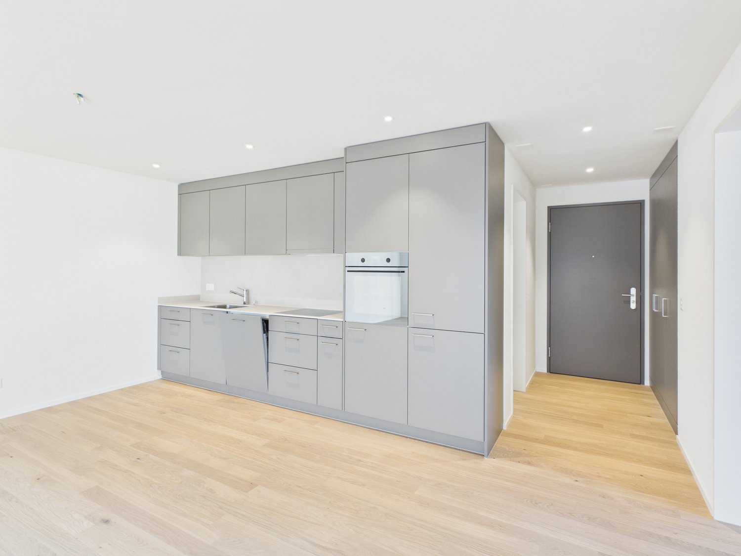 modern kitchen with integrated oven and sink, gray cabinetry, wooden floors, spacious, no appliances seen