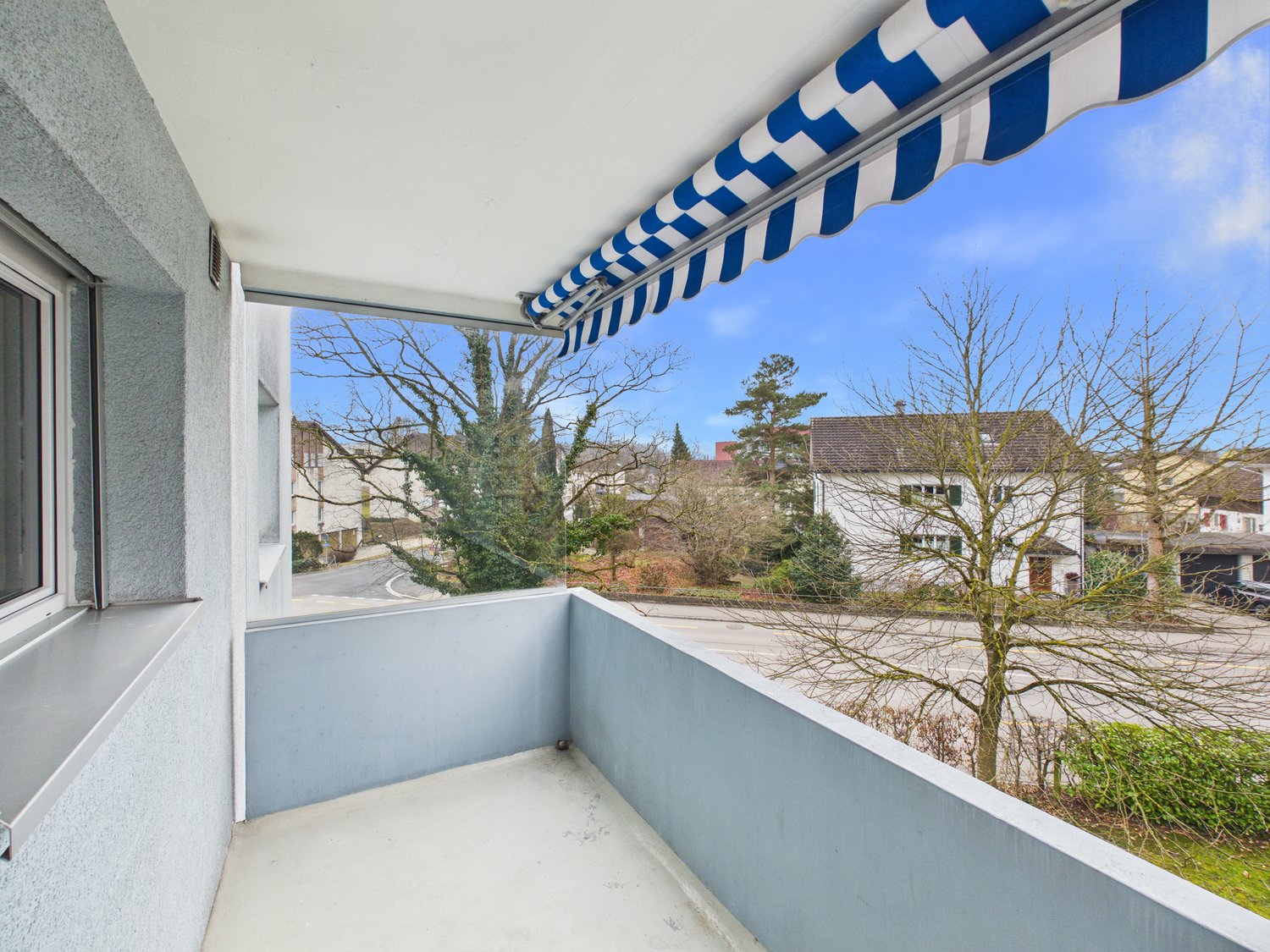 large balcony, blue and white striped awning, glass railing, road view