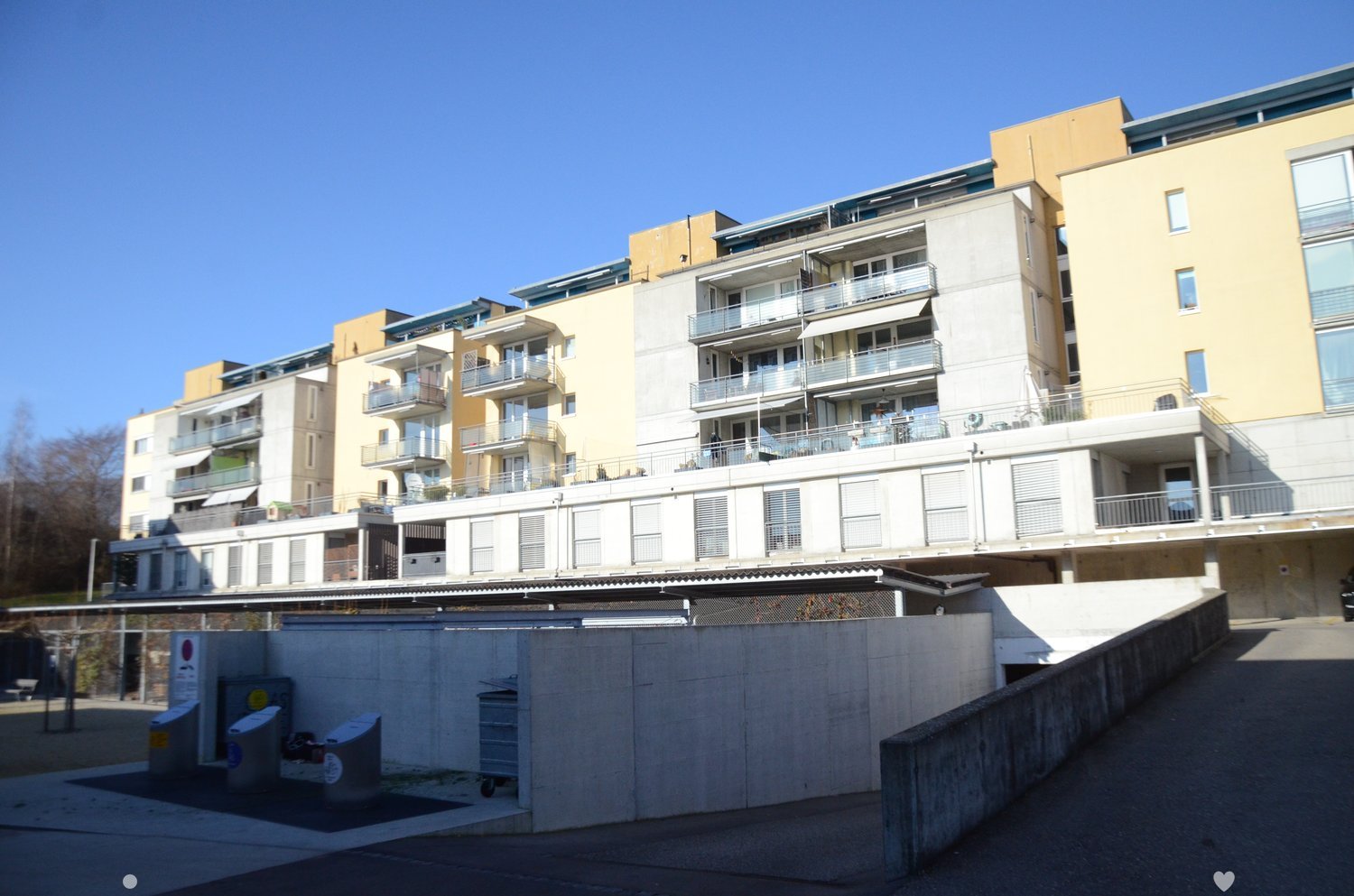 Apartment building with multiple floors, balconies, windows, and a ground floor wall