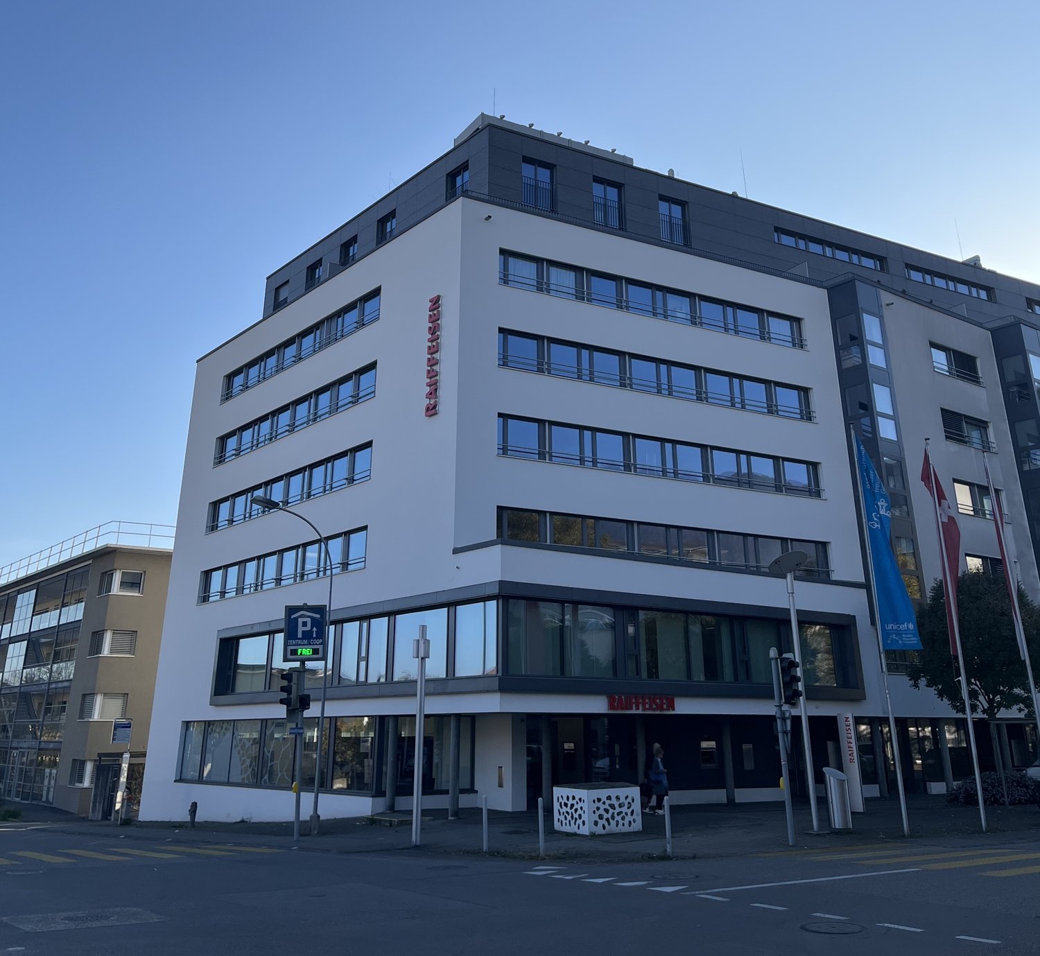 Commercial building, large windows, glass doors, 5 stories, blue sign, flags, banners