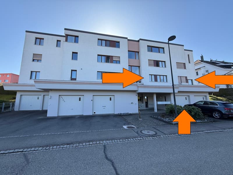 Three-story building, multiple garages in front, modern design, paved parking area