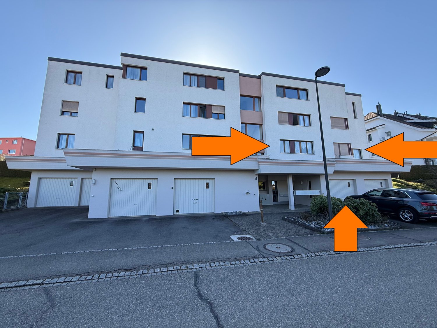 A multistory building with garages, a street light, and a car parked in front.