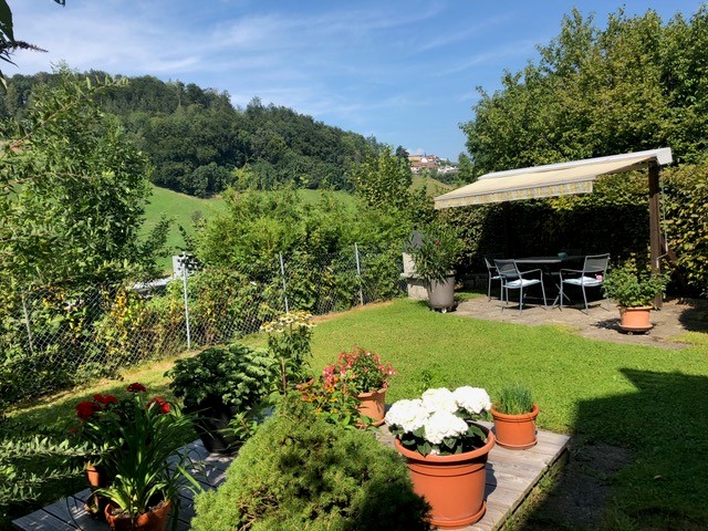 garden with seating area, dining table, canopy, greenery, lawn, and distant hills