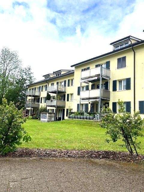 Apartment building, yellow exterior, many balconies, garden, trees
