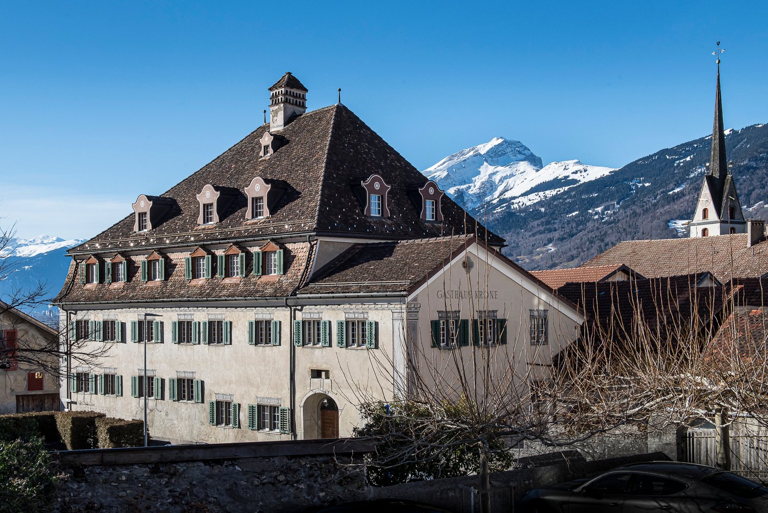 large building with multiple windows, brown roof, stone walls, surrounded by mountains