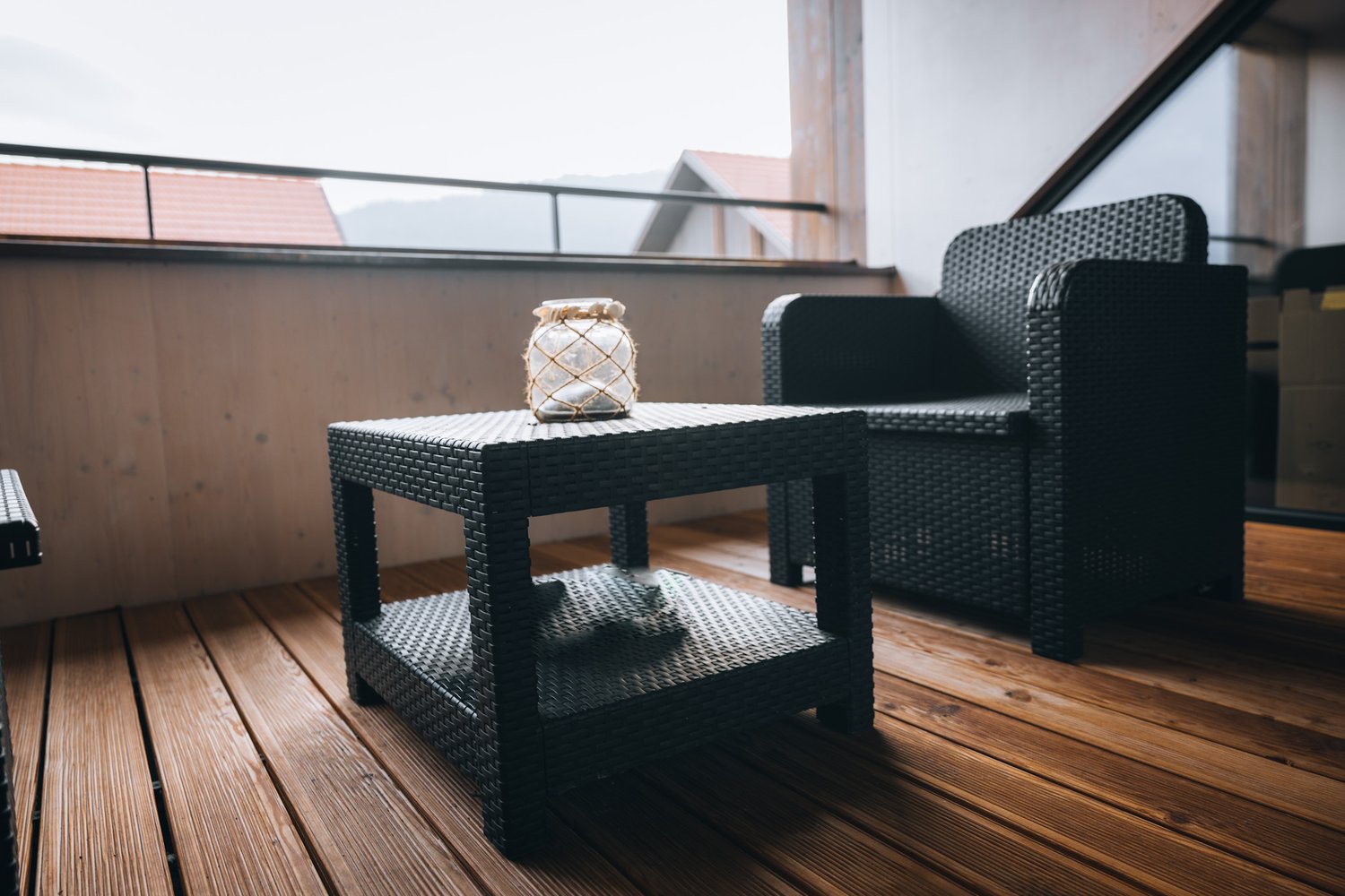 Black wicker outdoor furniture, tea table, a wicker chair, a glass vase, and a deck