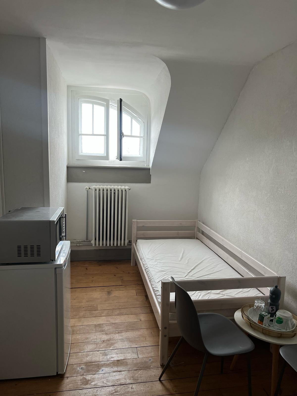 Small bedroom with a single bed, wooden floor, and a washing machine.