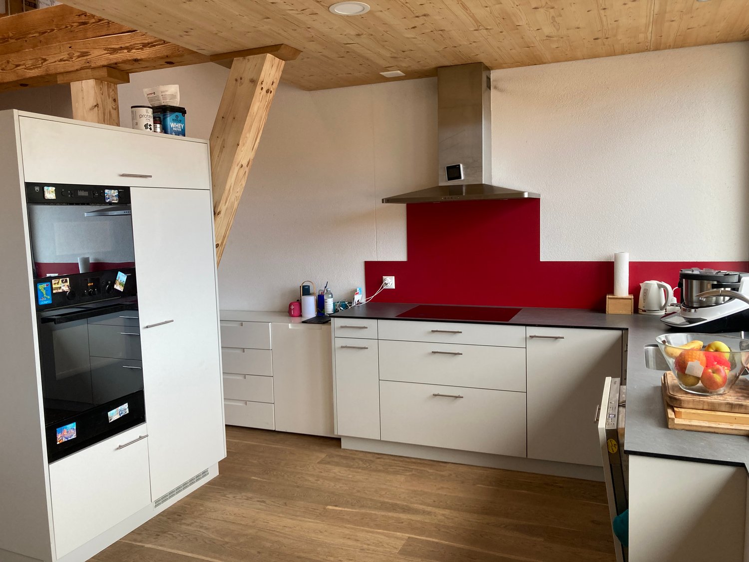 Spacious kitchen with wooden ceiling, white cabinets, red backsplash, built-in dishwasher, and various kitchen appliances and accessories