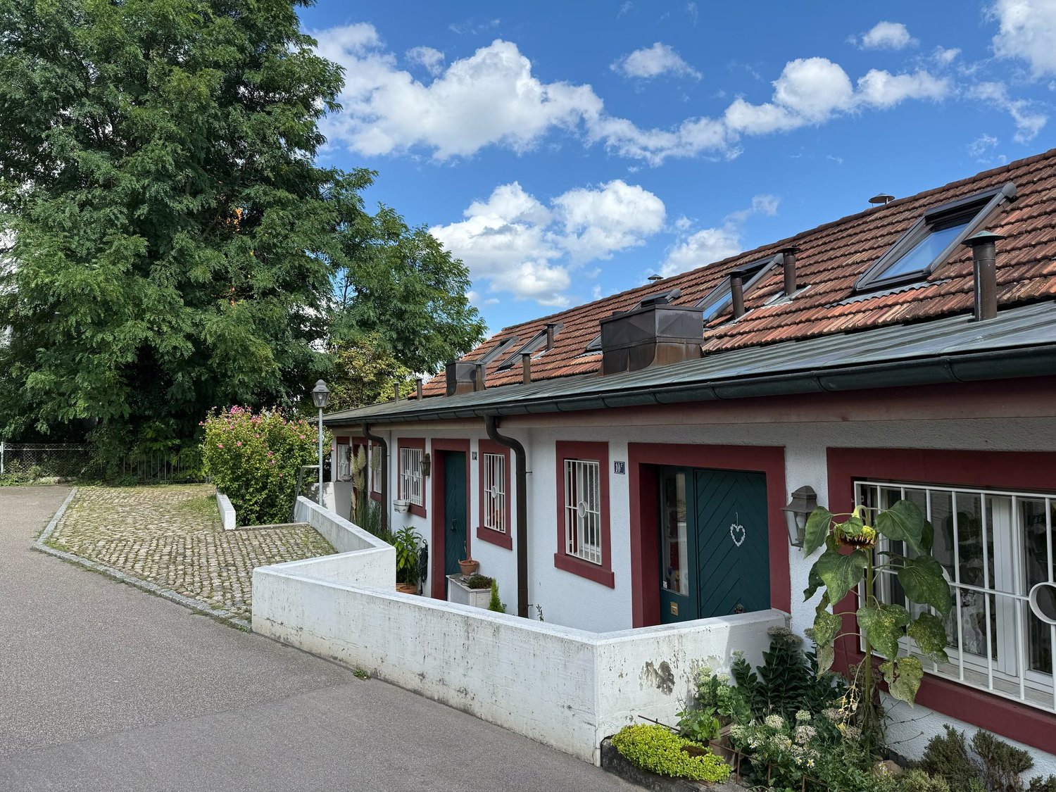 Detached building, red roof, white walls, red trim, green doors, several windows, small garden, plants, street lamp