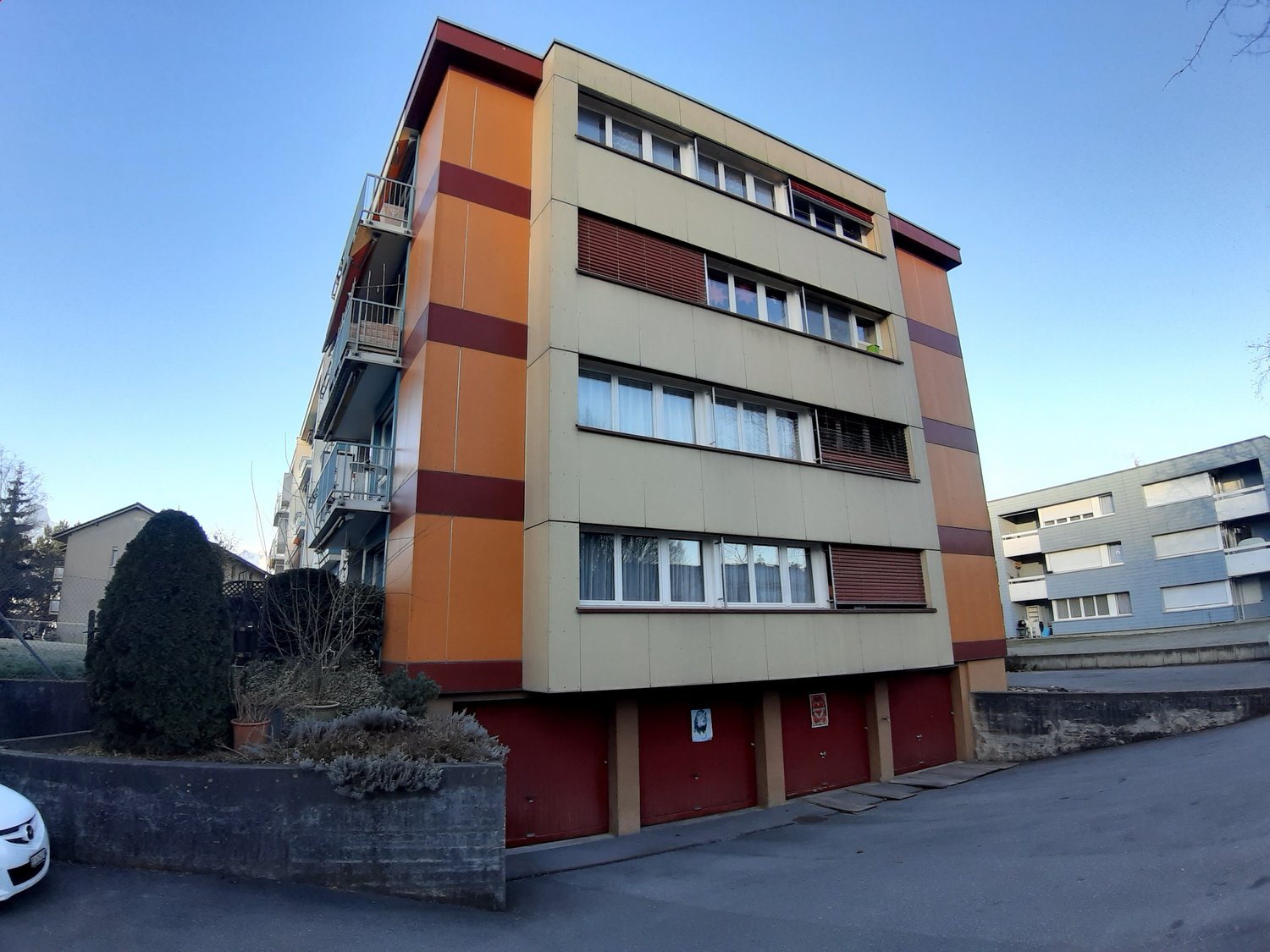 modern apartment building, orange and brown stripes, multiple windows, metal balconies, garages, parked car