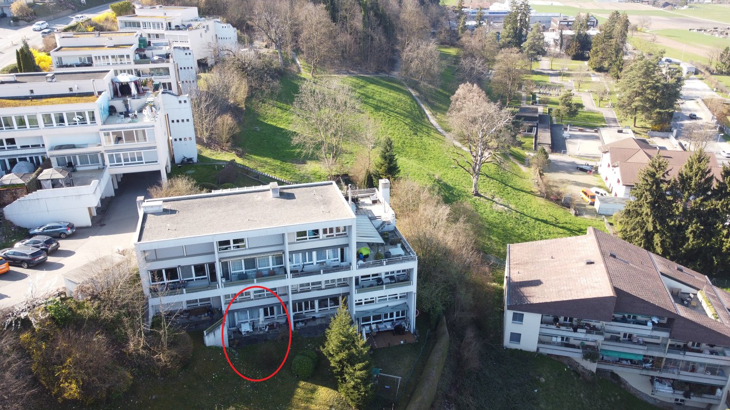 Aerial view of a white apartment building with multiple floors, balconies, and a red circle highlighting a specific area.