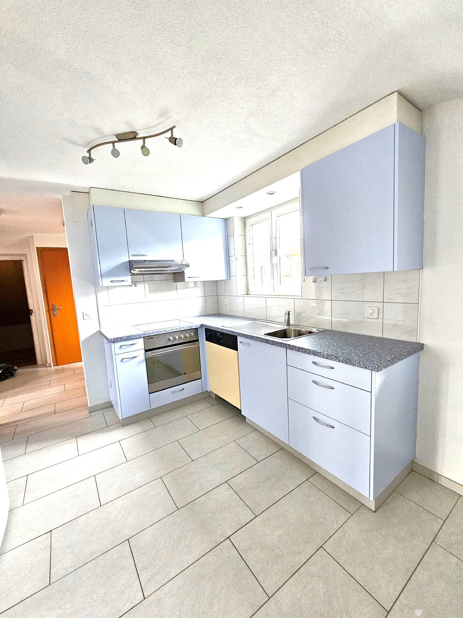 Modern kitchen with white cabinets, granite countertops, tiled floor, oven, and dishwasher