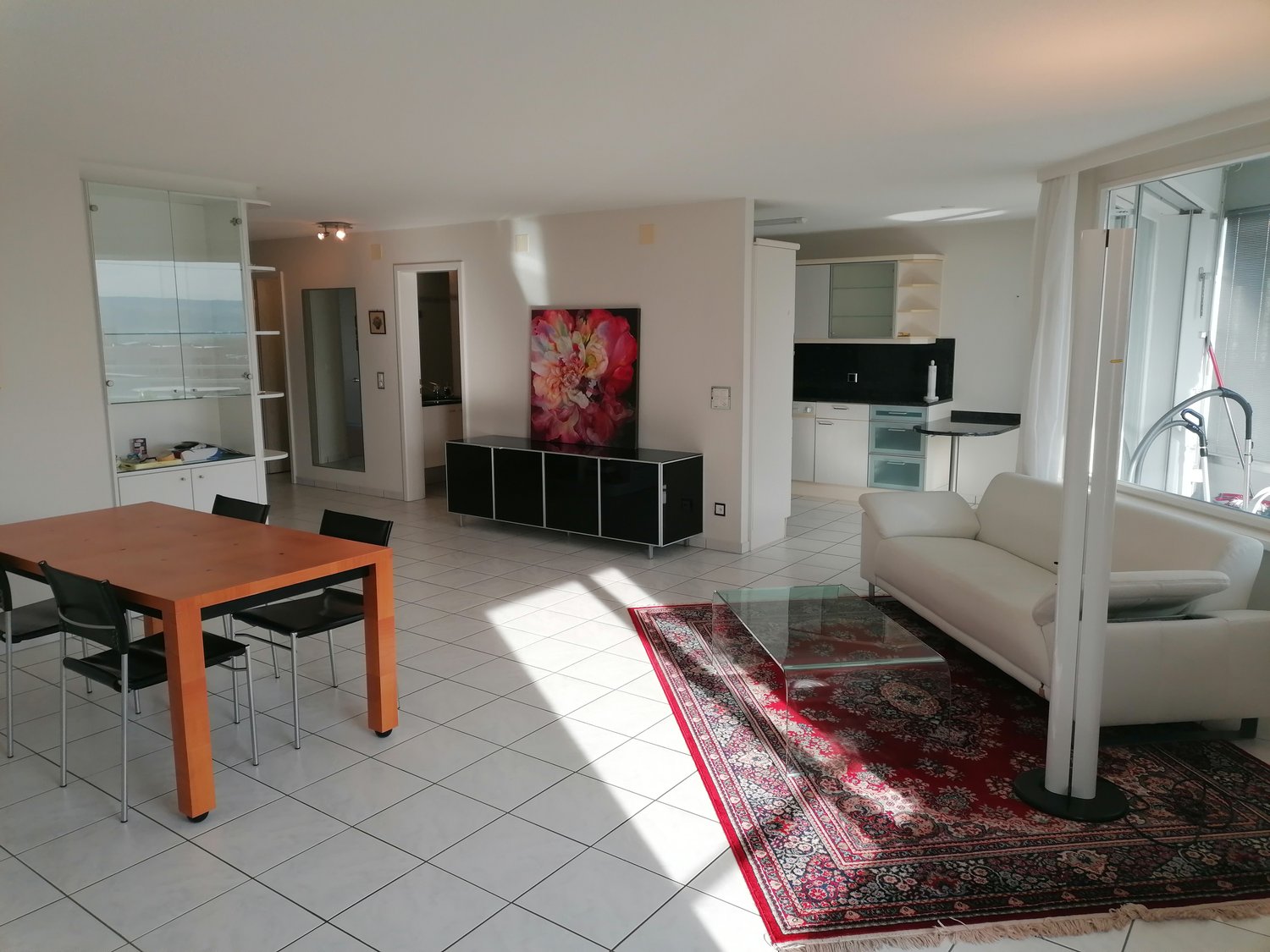 modern living room, white tiles, wooden dining table, white couch, glass coffee table, artwork, large windows, rug