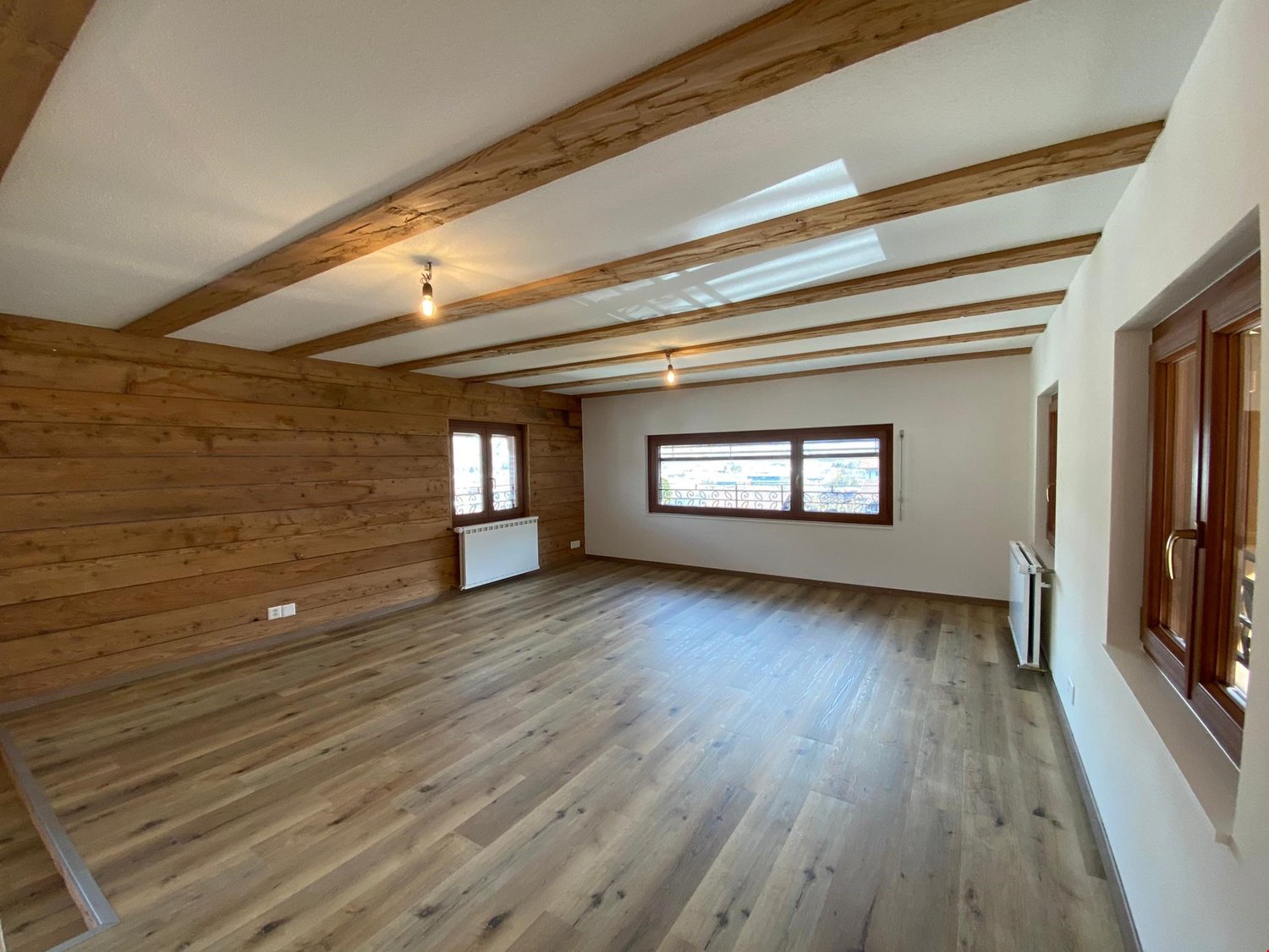 room with wooden walls, wooden ceiling beams, two radiators, three windows, wooden flooring