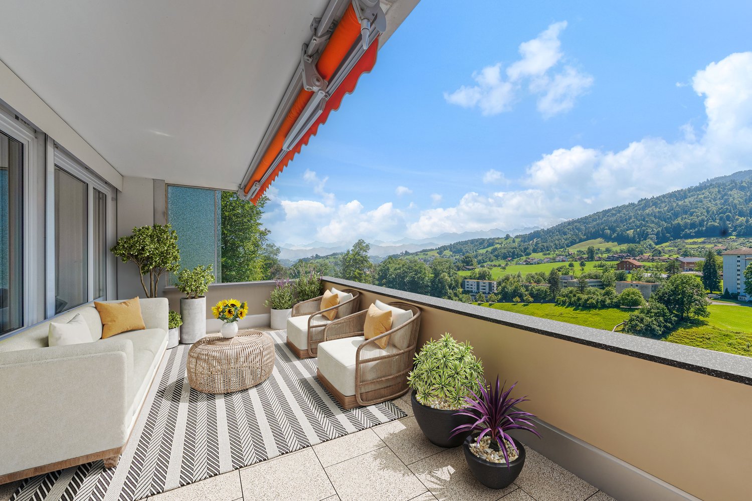 Spacious balcony with comfortable seating area, potted plants, and a stunning view of the surrounding mountains and countryside