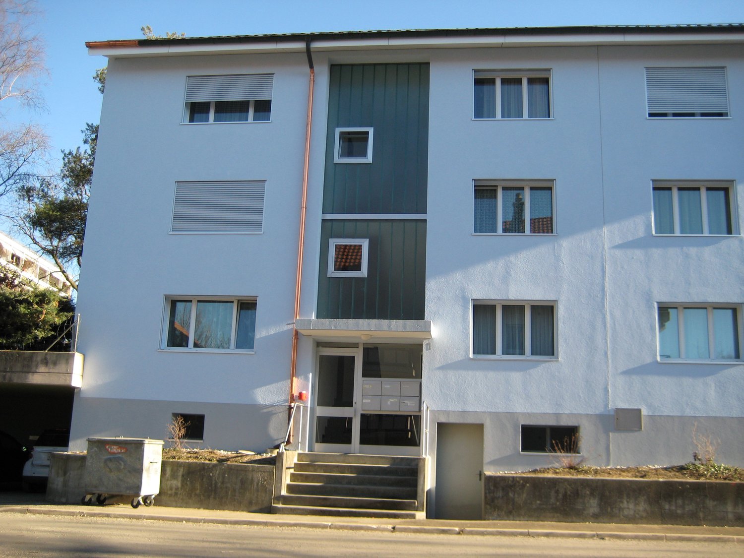 3-story apartment building, white painted walls, glass windows, central entrance with stairs, small concrete planters