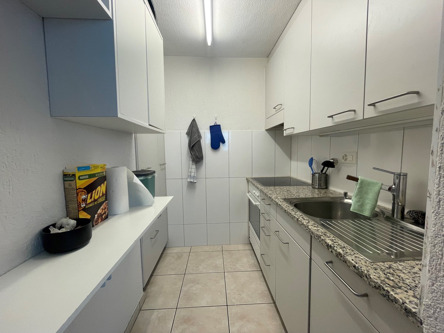 clean kitchen, tile flooring, stainless steel sink, countertop, cabinets, power outlet, towel, box on the counter
