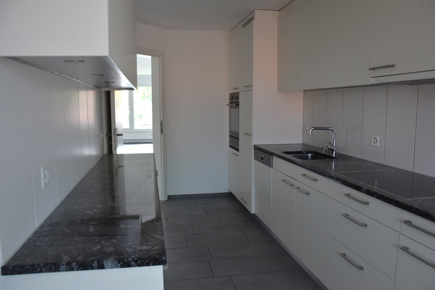 Modern kitchen with white cabinets, black granite countertops, stainless steel appliances, white tiled floor, under cabinet lighting