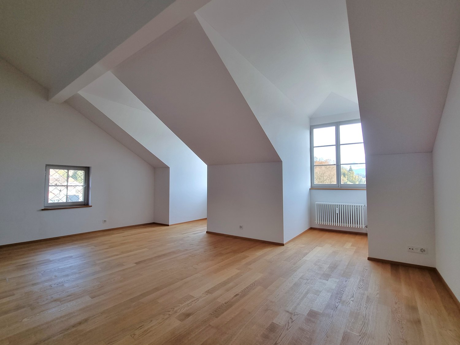 A empty room with hardwood floors, white walls, and two windows.