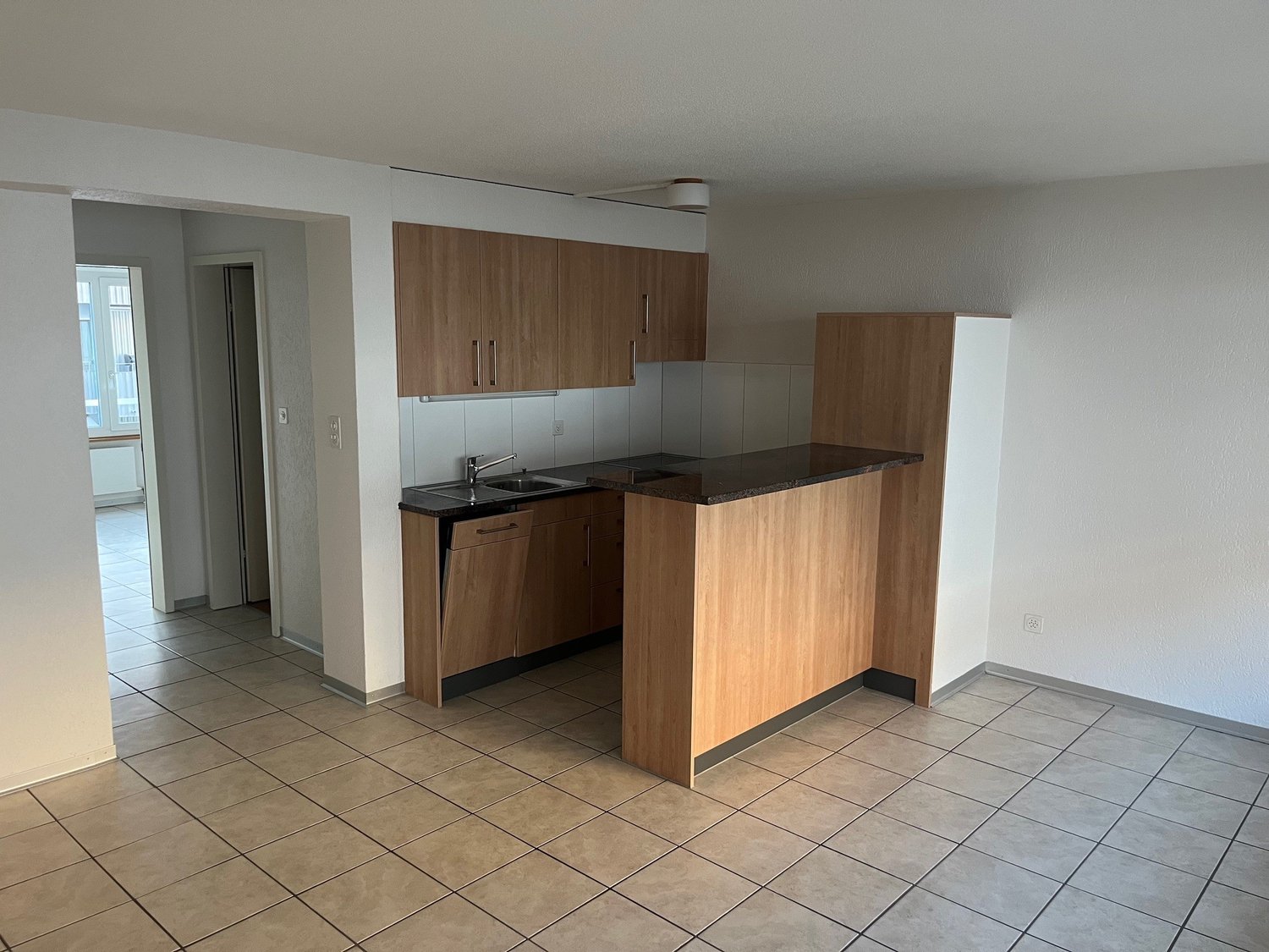 modern kitchen with wooden cabinets, black countertop, tiled floor, white walls, sink with faucet, and a power outlet