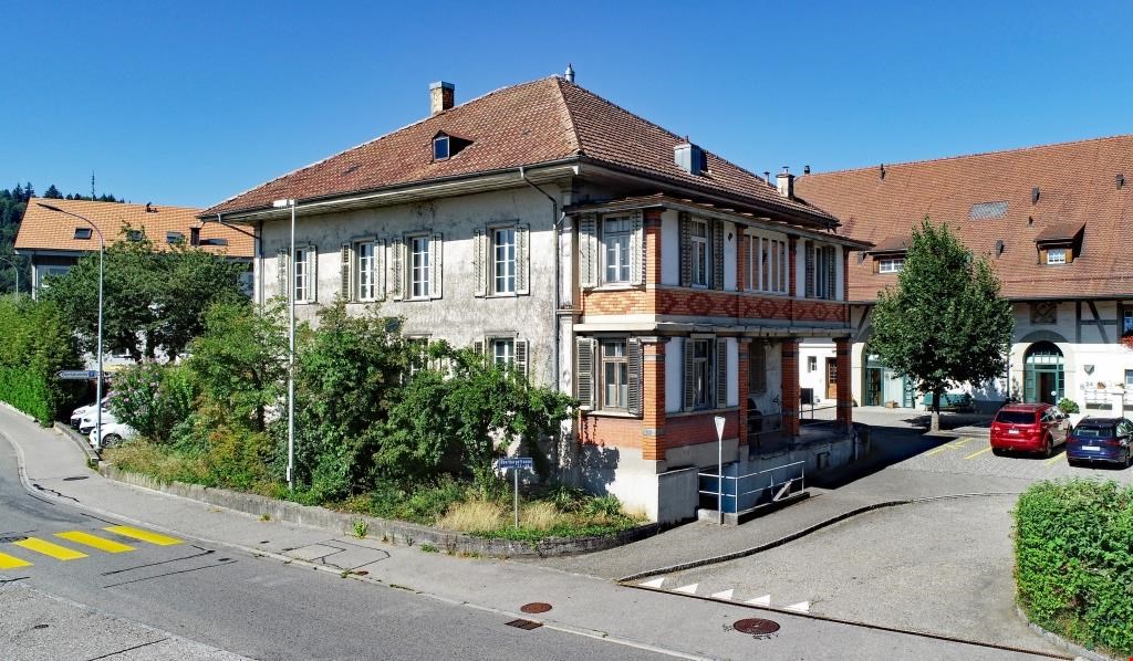 old house, brick and wood architecture, red roof, several windows, plants, parked cars