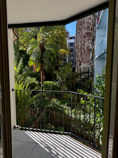 View of the garden and surrounding buildings from the balcony, metal railing, tiled floor