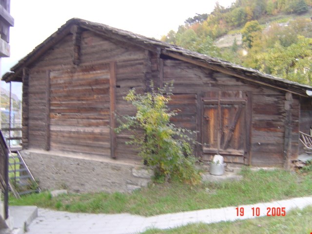 Old wooden cabin with a slanted roof, wooden walls, and a garage or storage area attached to the side.
