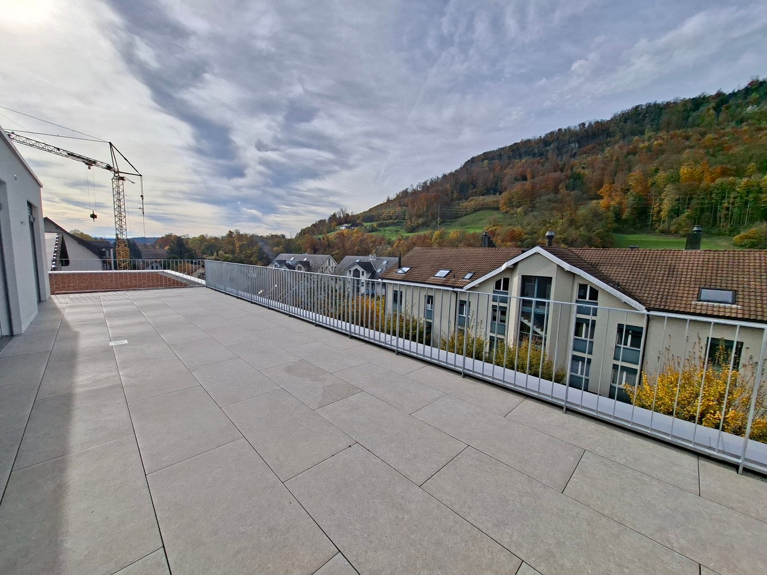 Rooftop terrace with tiled flooring, metal railing, mountain view, greenery, cloudy sky