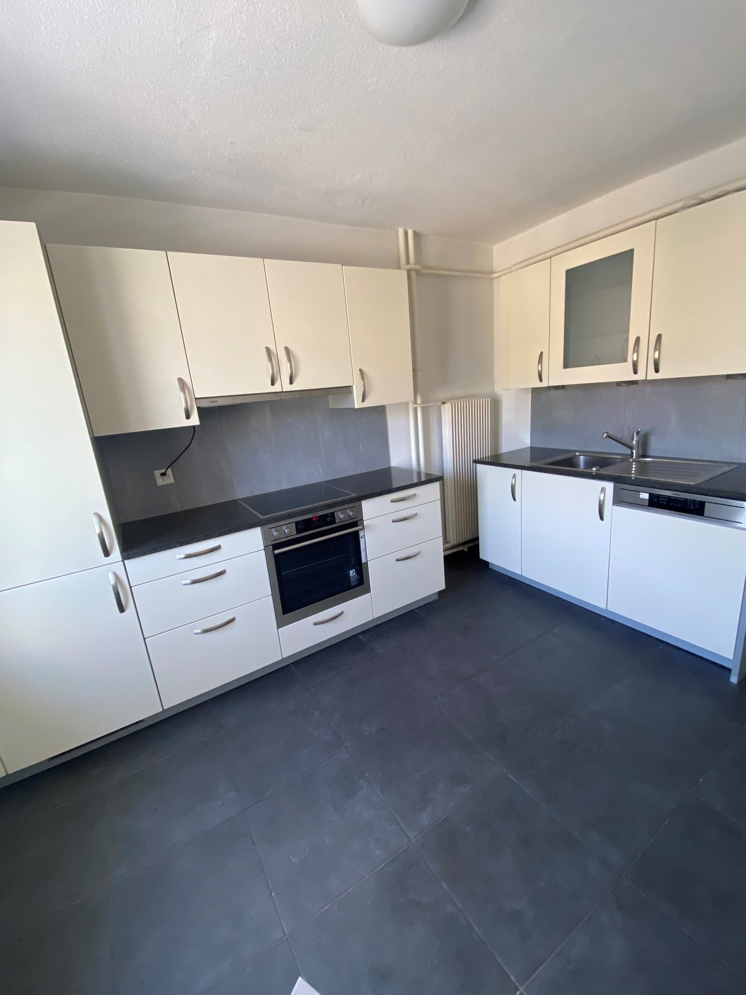 modern kitchen with all white cabinets, black countertops, integrated dishwasher, electric oven, and sink