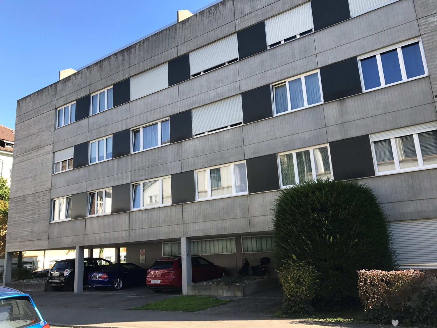 Apartment building with concrete facade, multiple floors, glass windows, and parking spaces beneath