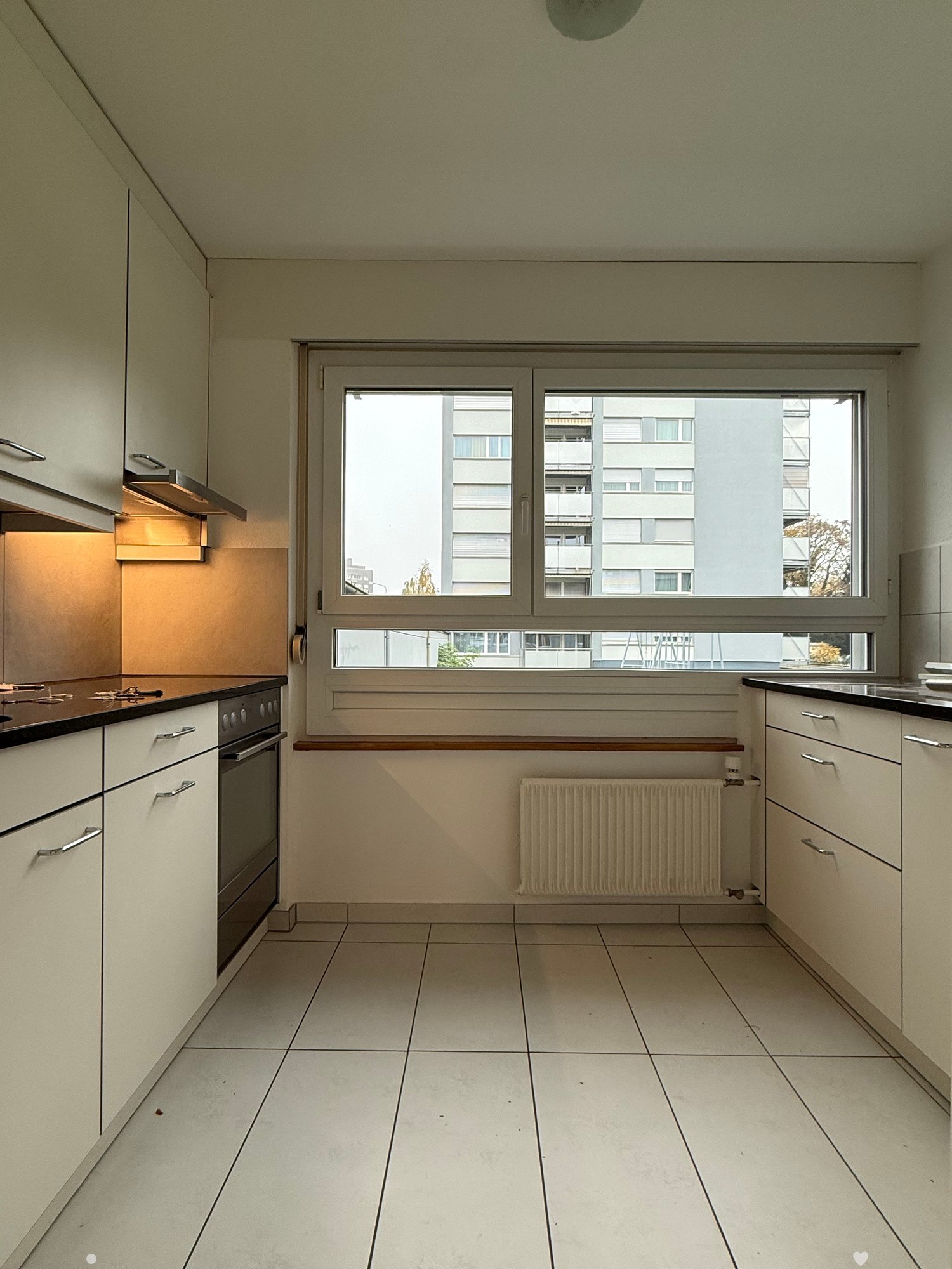 White tiled kitchen with a large window overlooking the outside