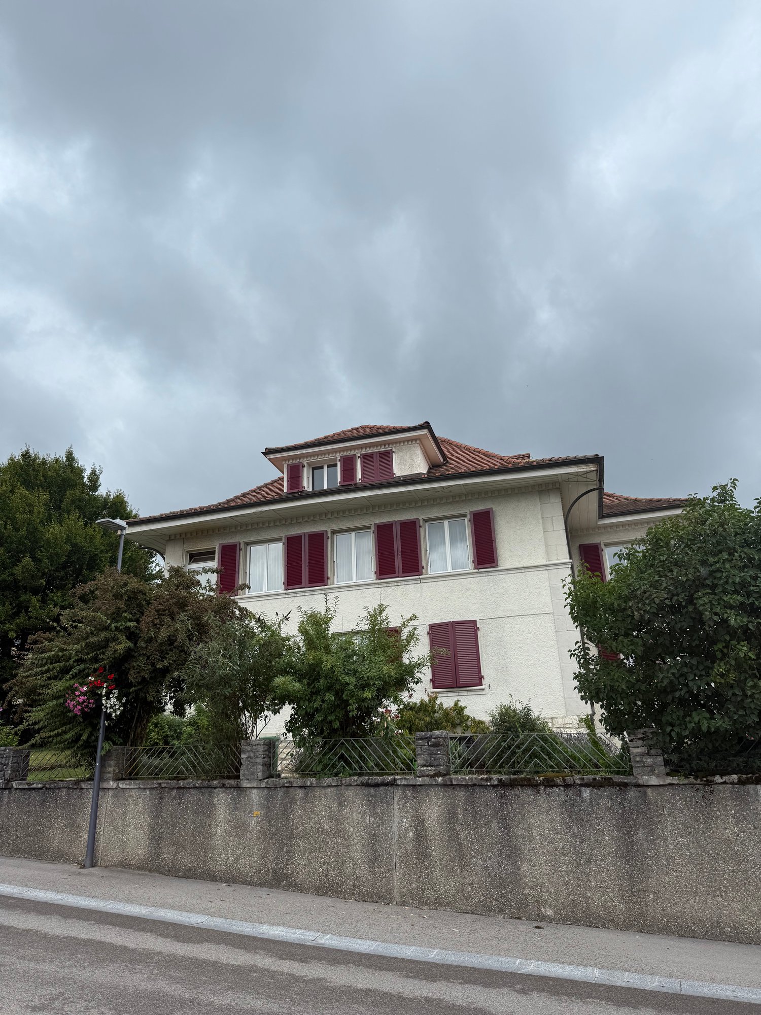 2 story house, white walls, red shutters, red roof, concrete fence, street lamp, trees
