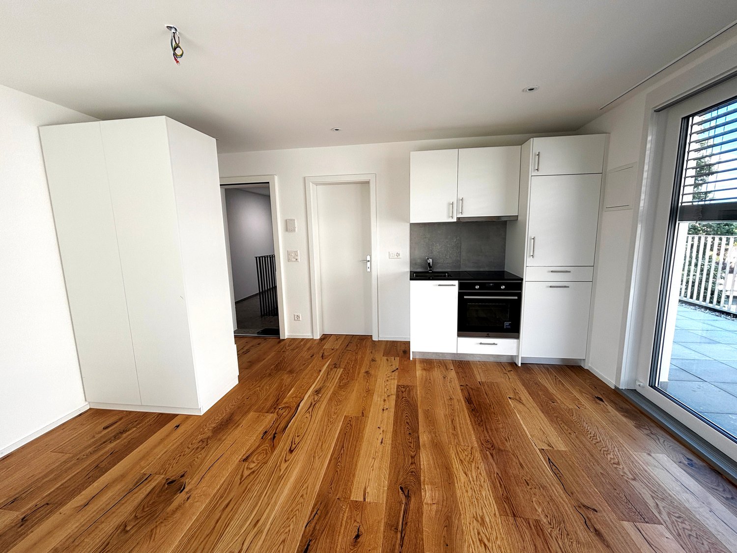 modern kitchen with white cabinets, wooden floor, sliding glass door to balcony
