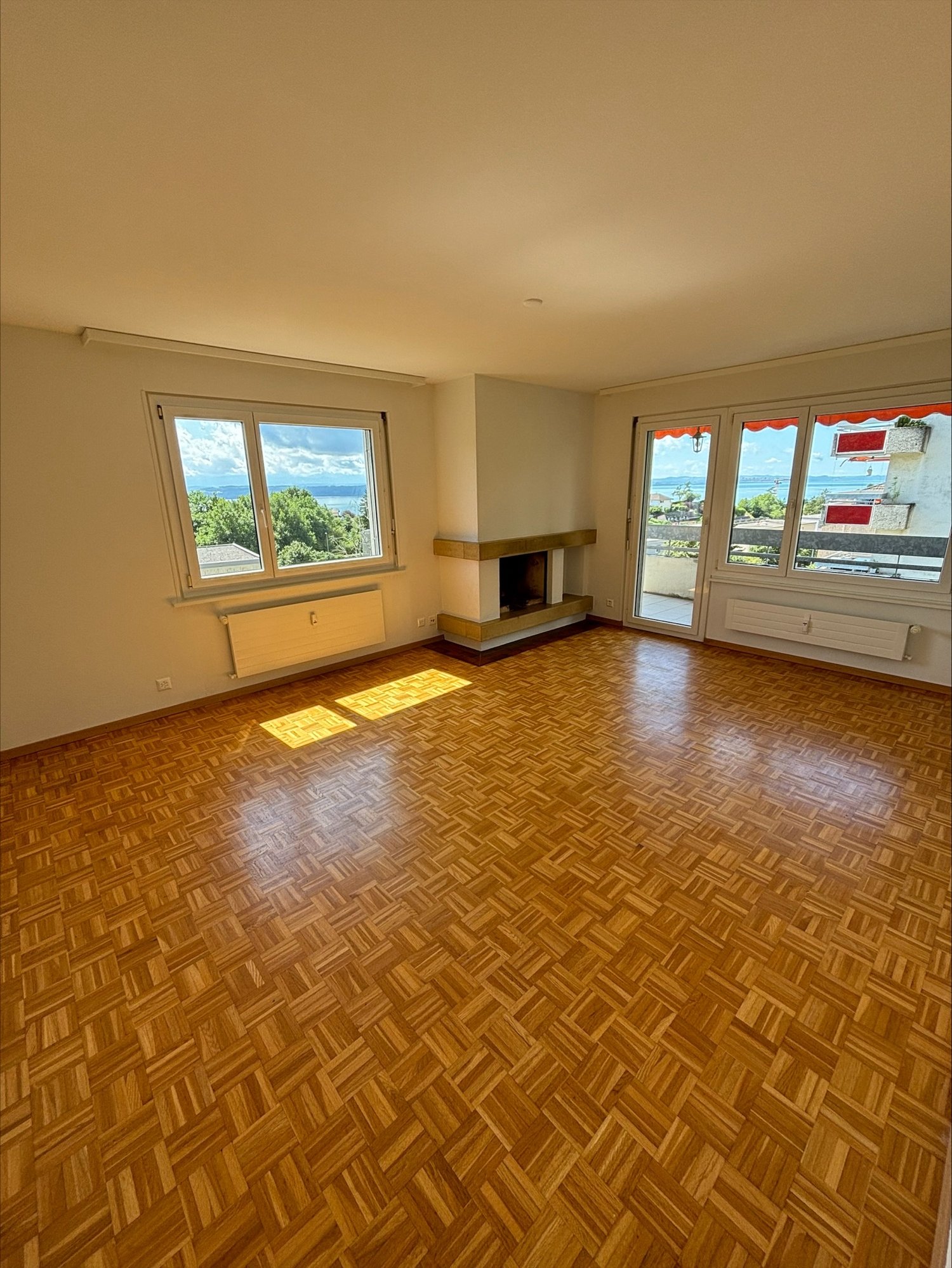 Spacious living room with large windows offering a scenic view, hardwood parquet flooring, and a fireplace.