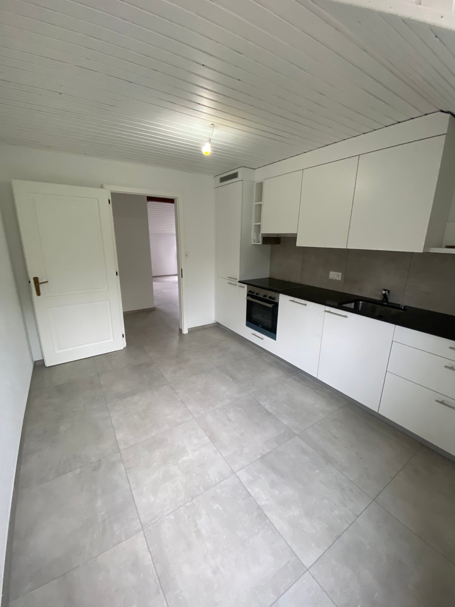 Modern kitchen with white cabinets, black countertops, and gray tile flooring. The kitchen includes a built-in dishwasher.
