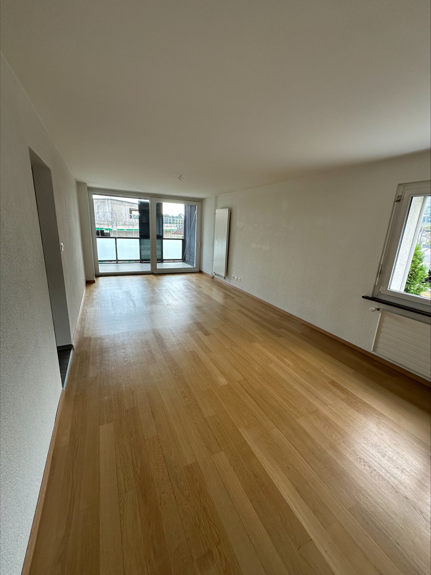 empty room with wooden floors, sliding glass doors to balcony, large windows, white walls, white ceiling, white heater