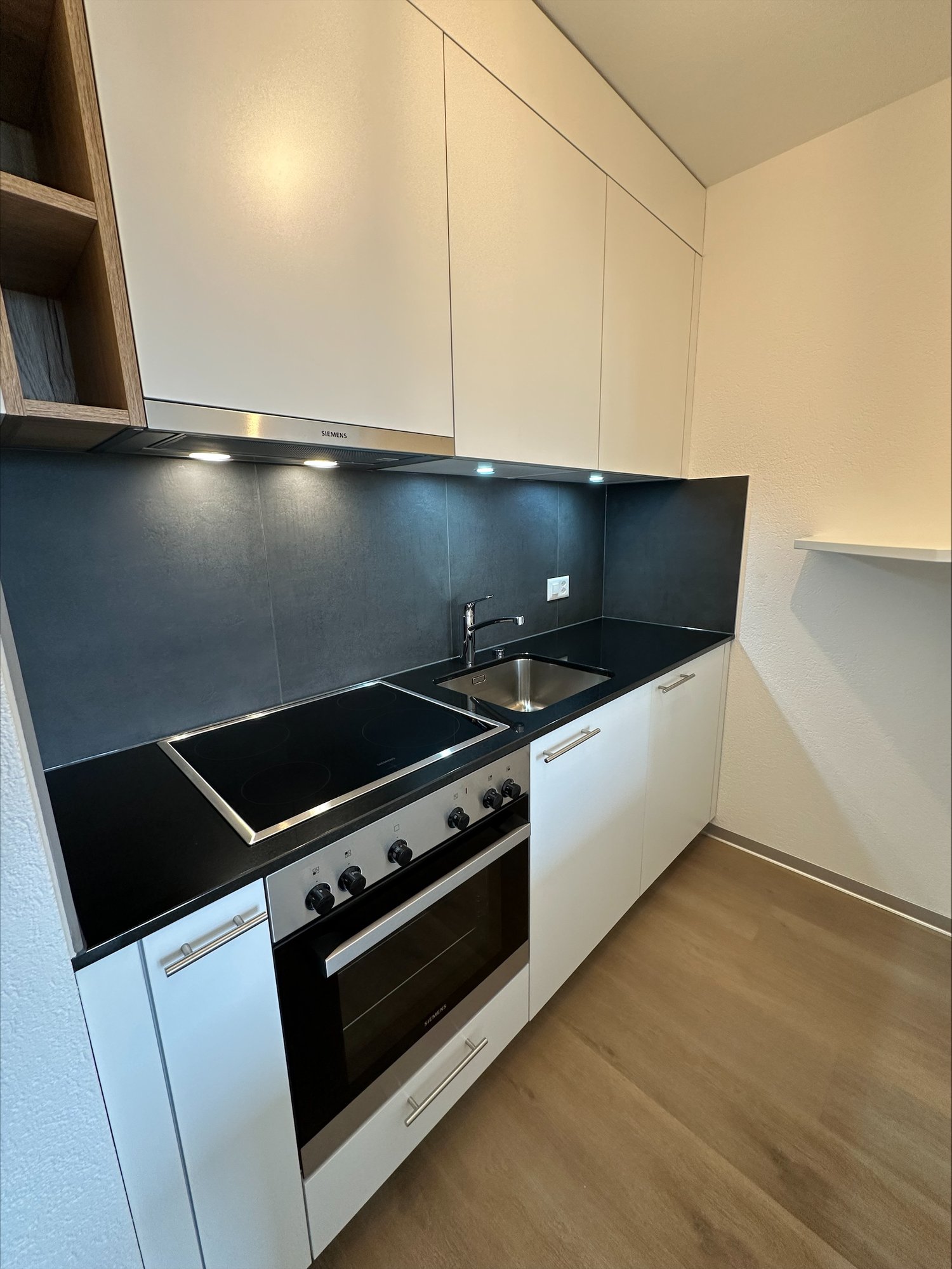 modern kitchen, black countertops, induction hob, dishwasher, white cabinets, wooden floor, sink with faucet, stainless steel hood