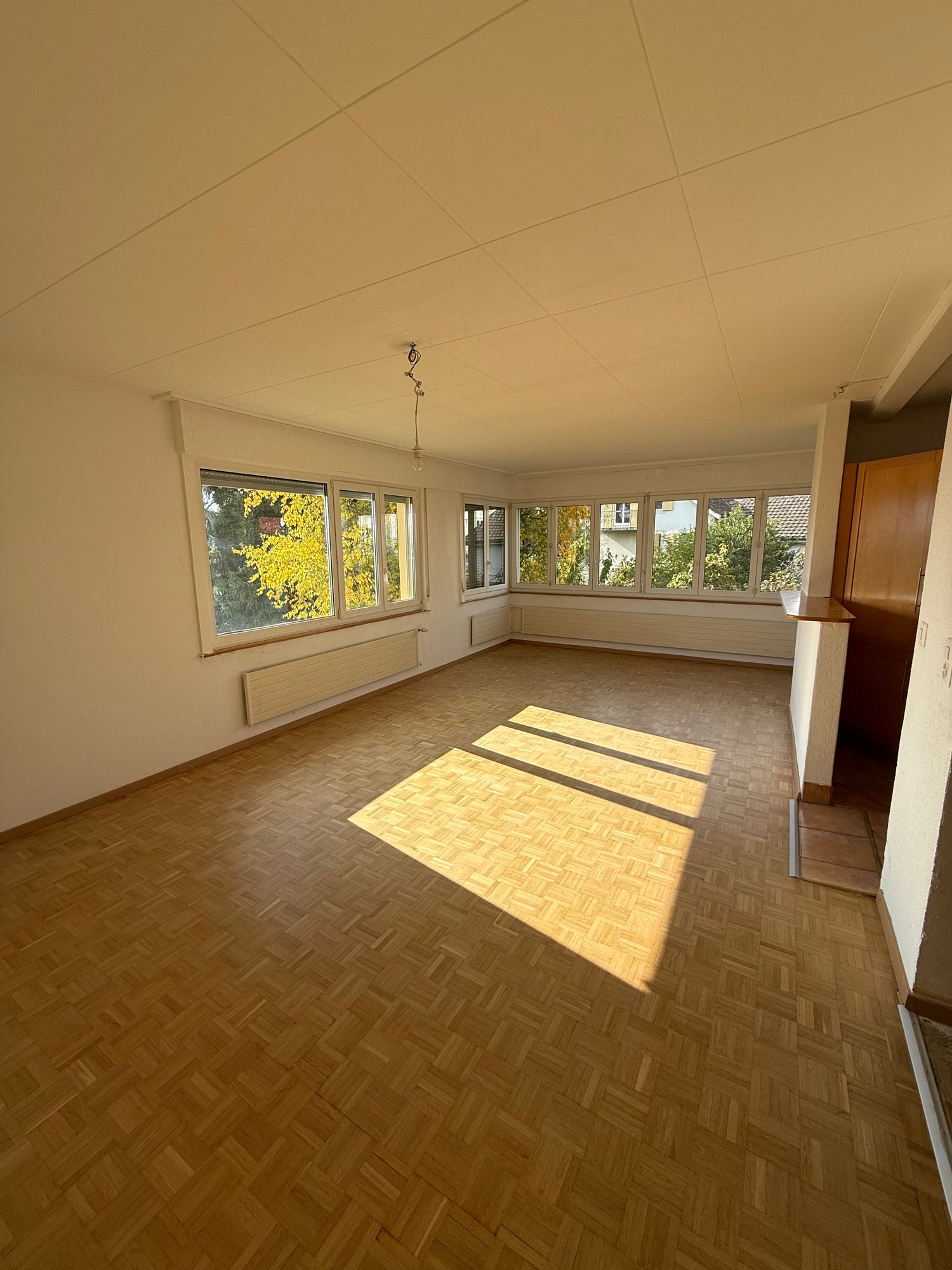 large empty room, large windows, wooden floor, beams on ceiling